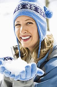 Woman wearing blue ski cap and gloves holding snow
