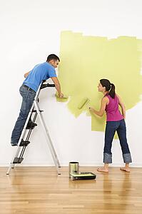 Attractive young adult couple painting interior wall of house.
