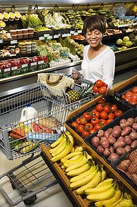 Smiling middle aged African American woman selecting tomatoes from grocery store produce.