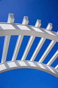 Low angle view of arched white trellis with blue sky.