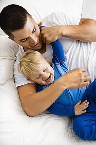 Toddler boy and father playing and tickling in bed
