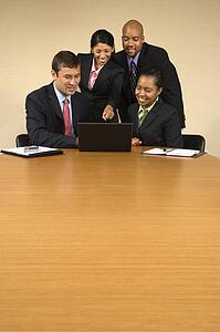 Businesspeople gathered around laptop computer looking at monitor and smiling.