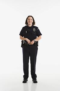 Portrait of mid adult Caucasian policewoman standing with hands on gun holster looking at viewer smiling.
