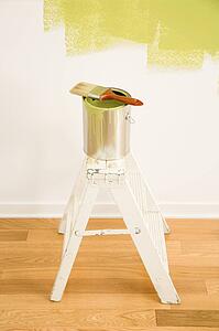 Paintbrush on can on top of step ladder with painted wall.