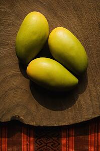Still life of three wooden mangoes on plate.