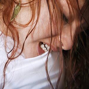 Close up of pretty young redhead woman biting pillow.