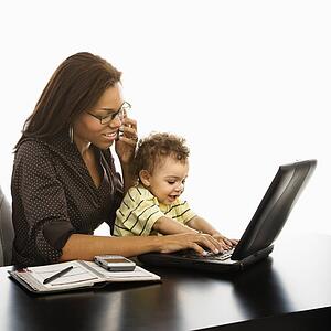 Businesswoman at work on laptop and cell phone with toddler son on lap