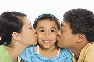 Mother and father kissing opposite cheeks of smiling daughter