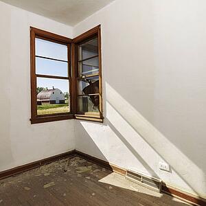 Empty abandoned room with sunrays stretching across wall from corner window