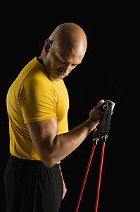 Mid adult multiethnic man wearing yellow exercise shirt exercising with stretch band and looking at bicep.