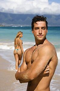 Man standing on beach with woman in background