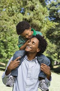 Father carrying son on shoulders in park.
