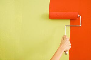 Caucasian female hand painting red over a green wall with a paint roller.