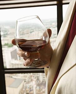 Man in suit holding snifter of brandy.
