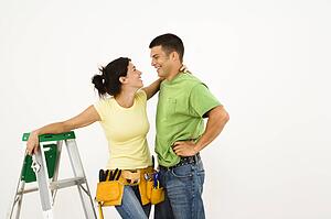 Couple with tools and ladder standing in home smiling
