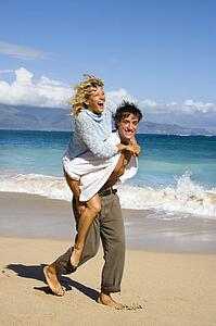 Woman riding piggyback on man while both smile and laugh on Maui, Hawaii beach