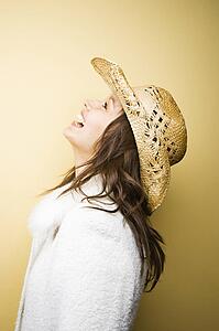 Profile of young adult woman wearing cowboy hat leaning backwards laughing