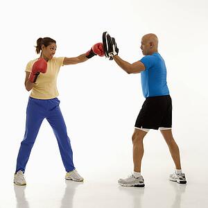 Mid adult woman standing and punching focus mitts worn by mid adult man.