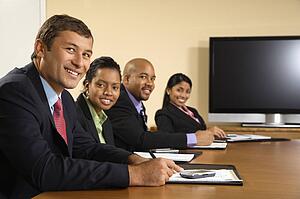 Businesspeople sitting at conference table smiling with flat screen 