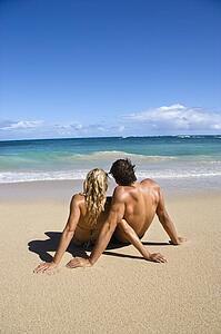 Couple sitting close together on Maui, Hawaii beach looking out at ocean.