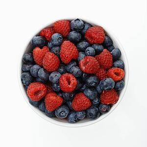 Bowl of mixed blueberries and raspberries on white background.