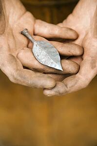Dirty male metal smith's hands holding metal leaf