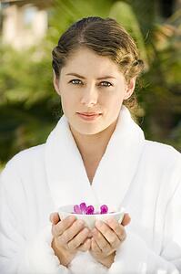 Attractive mid-adult woman in white robe holding bowl of purple orchids floating in water