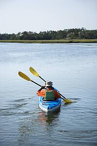 Back view of African American middle-aged couple paddling kayak.