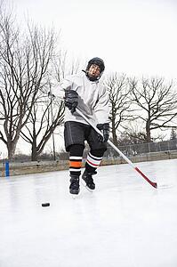 Boy in ice hockey uniform skating on ice rink moving puck.