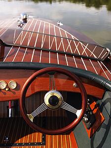 Wooden boat with steering wheel and dashboard floating in gentle water.