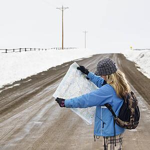 Young woman in winter clothes standing on muddy dirt road looking at map