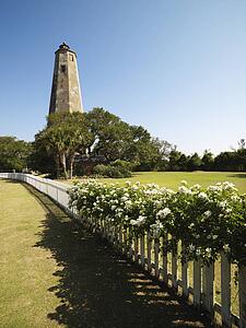 Bald Head Lighthouse with fence and wild roses at Bald Head Island, North Carolina.