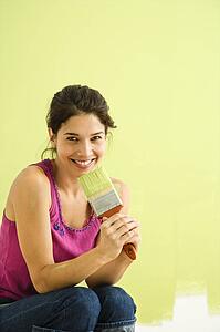 Woman kneeling in front of partially painted wall holding paintbrush