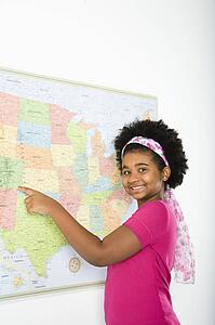 African American girl pointing to map of United States and smiling at viewer.