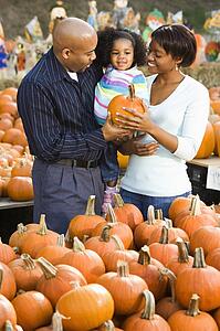 Parents and daughter picking out pumpkin and smiling at outdoor market.