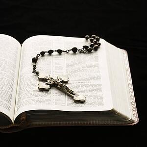 Rosary with crucifix lying on open Bible.