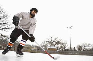 Boy in ice hockey uniform skating on ice rink moving puck