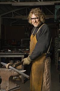 Male metalsmith holding metal on anvil