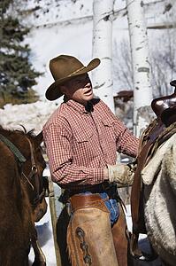 Male wrangler putting saddle on horse