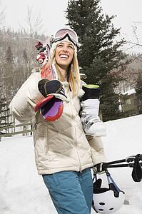 Pretty blond young woman carrying ski equipment in snow and smiling