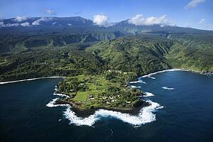 Aerial of rocky coast on Pacific ocean with mountains in background in Maui, Hawaii.