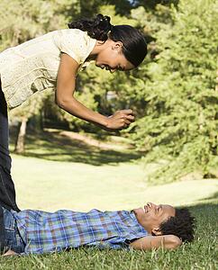 Woman standing over smiling man laying in grass taking his photograph.