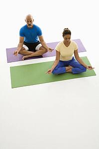 Mid adult man and woman sitting in lotus position on exercise mats with eyes closed and legs crossed