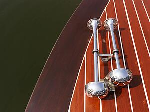 Detail of dual chrome trumpet horns on wooden boat floating in water.