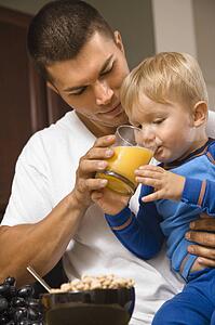 Man helping toddler son drink juice