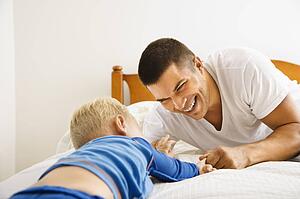 Toddler boy and father playing in bed
