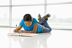 Preteen girl laying on floor doing homework