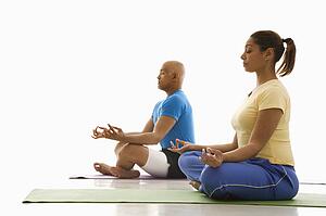Side view of mid adult man and woman sitting in lotus position on exercise mats with eyes closed and legs crossed.
