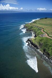 Aerial view of cars parked on rocky cliff with surfers below in Maui, Hawaii.