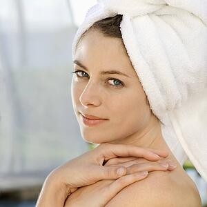 Mid-adult woman wearing towel around head with hands on shoulder looking at viewer